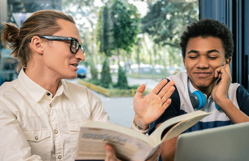 a teenage boy smiling, looking at an adult next to him.